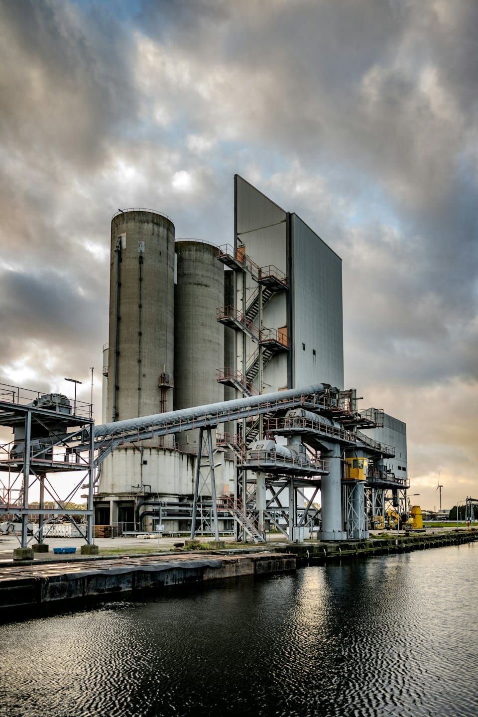 Stabilimento portuale industriale con silos e nastri trasportatori vicino a un canale.