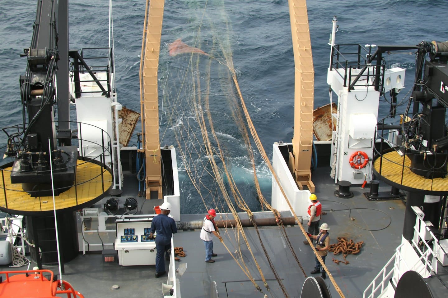Tecnici marini che calano una grande rete da un'imbarcazione in mare.