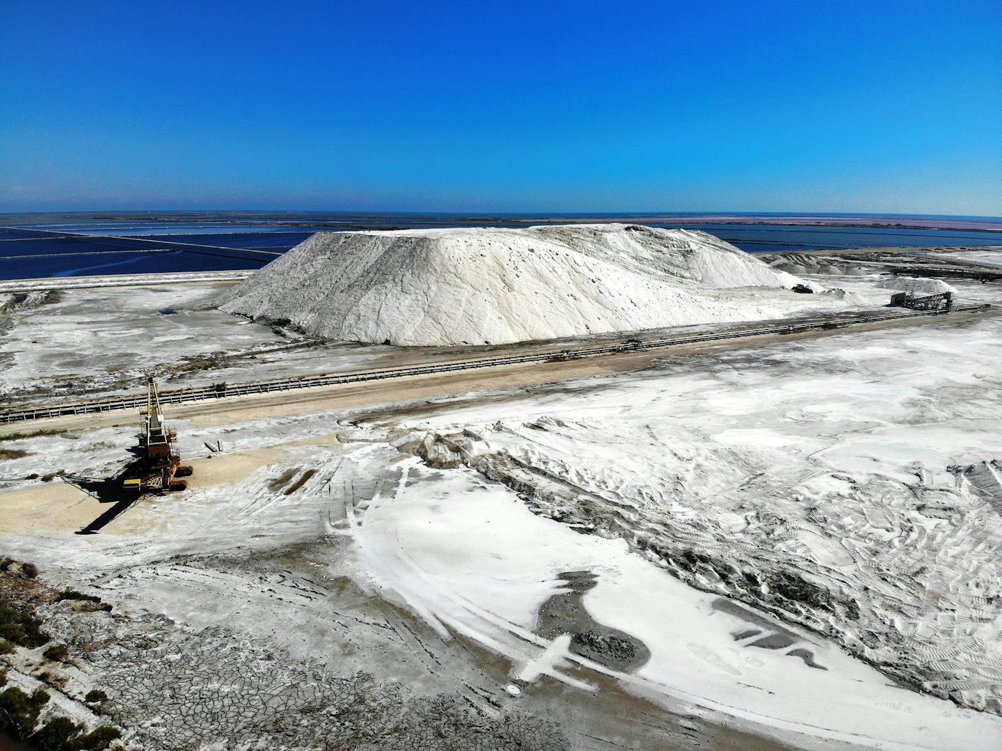 Un impianto industriale di sale presenta grandi cumuli bianchi e stagni di evaporazione colorati.